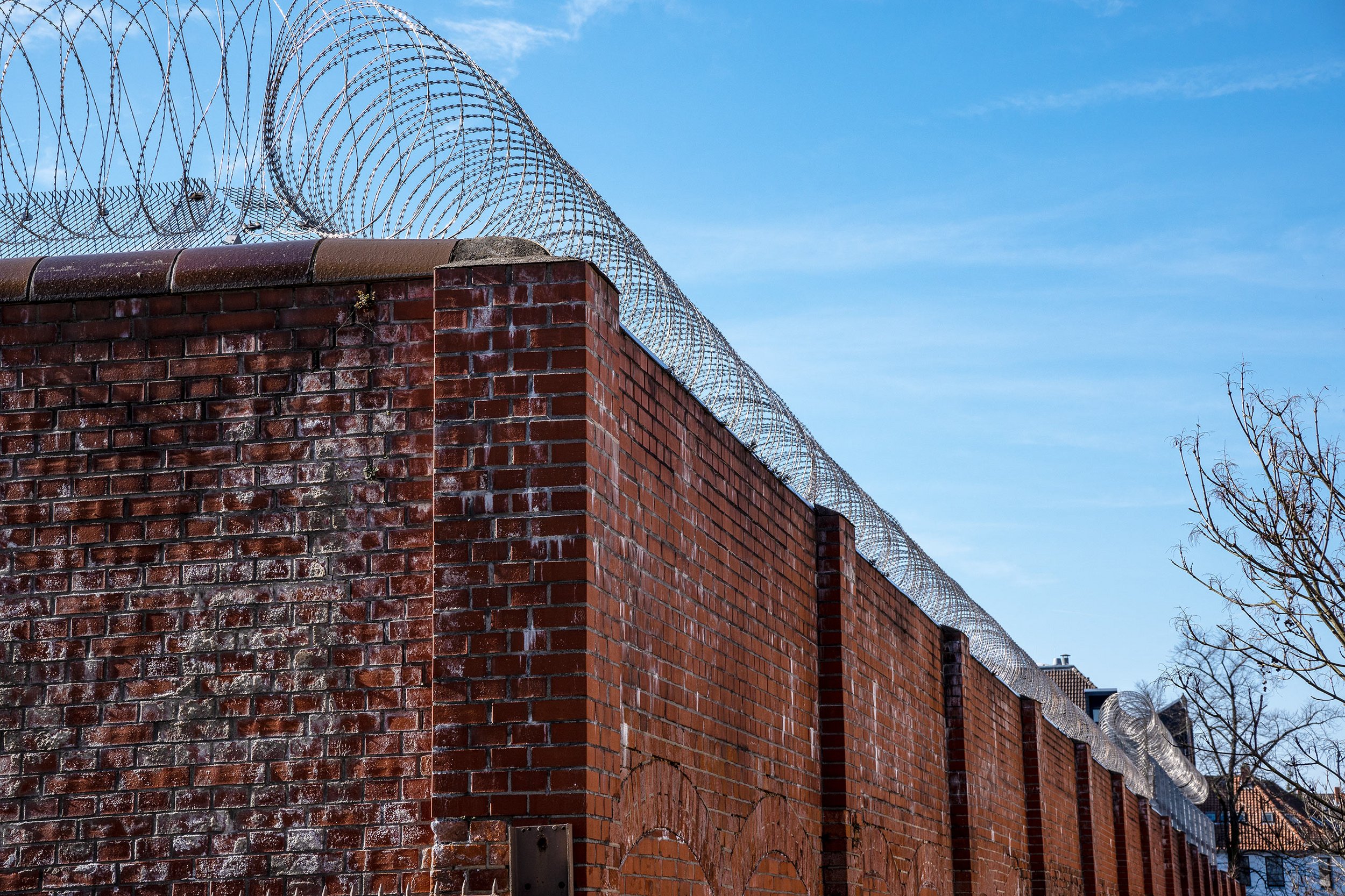 Gefängnismauer aus rotem Backstein mit aufgesetzter Stacheldrahtrolle