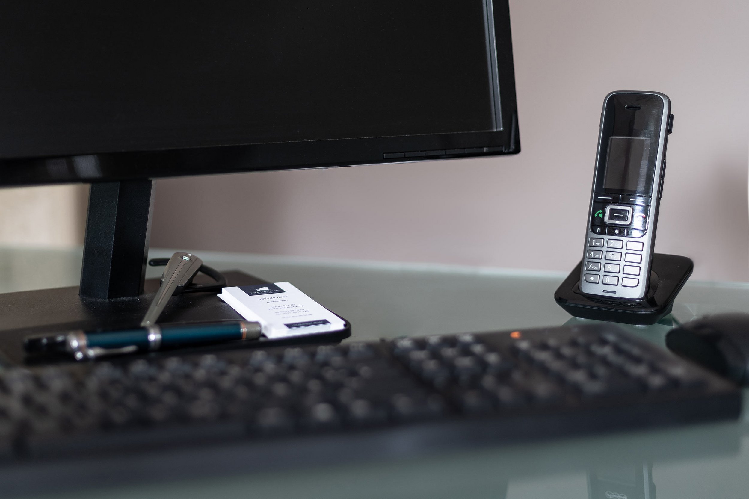 Detailansicht vom Schreibtisch mit Monitor im Anschnitt, Headset, und schnurlosem Telefon in der Ladestation
